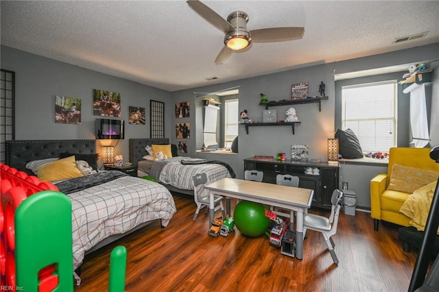 bedroom with a textured ceiling, ceiling fan, wood finished floors, and visible vents