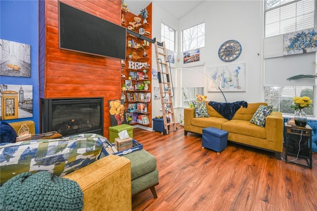 living room with a high ceiling, wood finished floors, and a glass covered fireplace