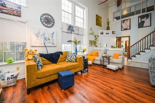 living area with stairway, wood finished floors, a towering ceiling, and a healthy amount of sunlight