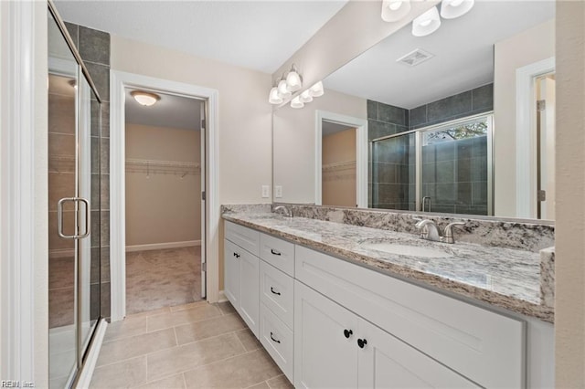 full bathroom with double vanity, a stall shower, tile patterned flooring, a walk in closet, and a sink