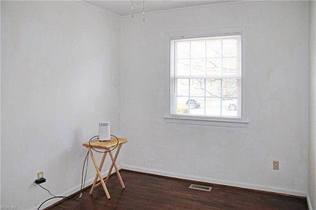 empty room featuring visible vents, dark wood-type flooring, baseboards, and ornamental molding