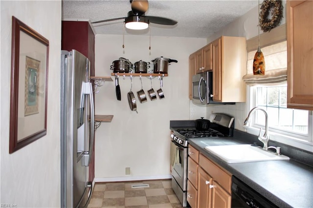 kitchen featuring dark countertops, light floors, appliances with stainless steel finishes, a textured ceiling, and a sink