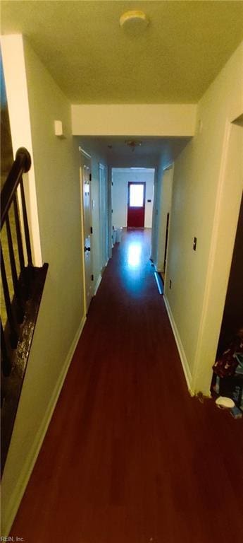 hall featuring a textured ceiling, baseboards, and wood finished floors