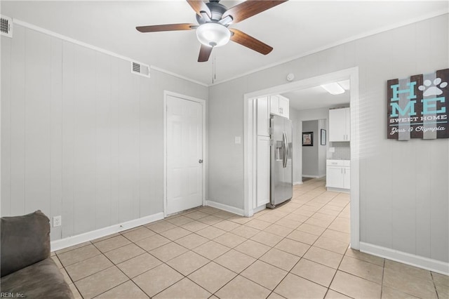 empty room featuring a ceiling fan, light tile patterned flooring, visible vents, and crown molding