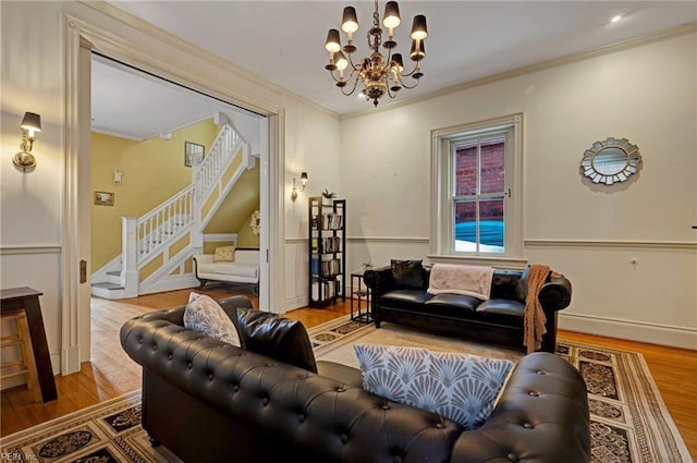 living room featuring wainscoting, wood finished floors, stairs, crown molding, and a notable chandelier