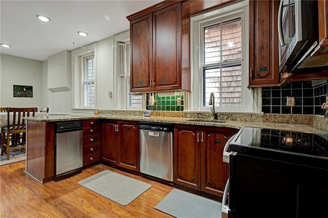 kitchen featuring tasteful backsplash, light wood-style flooring, appliances with stainless steel finishes, a sink, and a peninsula