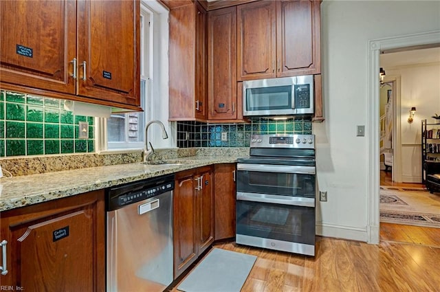 kitchen featuring light stone counters, a sink, appliances with stainless steel finishes, light wood-type flooring, and backsplash