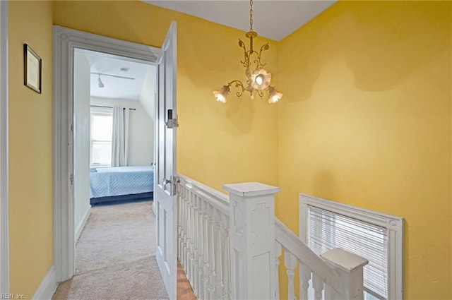 hall featuring lofted ceiling, light colored carpet, an inviting chandelier, an upstairs landing, and baseboards