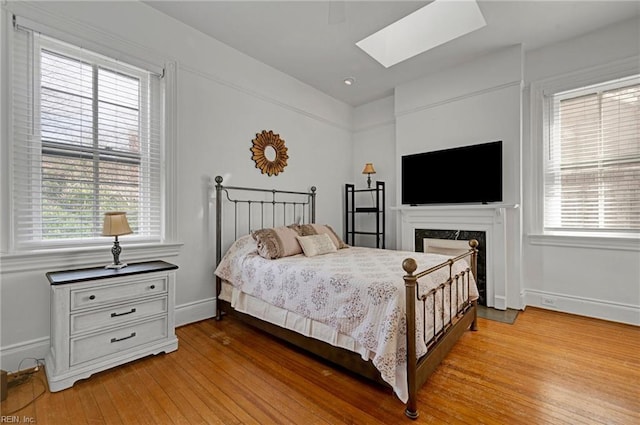 bedroom featuring multiple windows, a skylight, light wood-style flooring, and baseboards