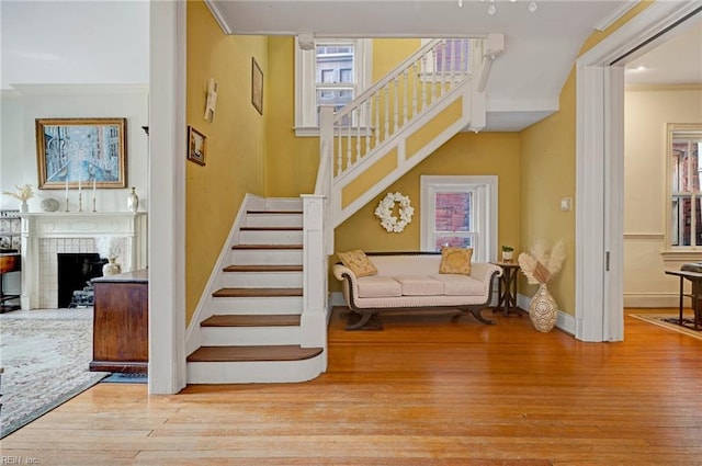 staircase featuring plenty of natural light, a fireplace, crown molding, and wood finished floors