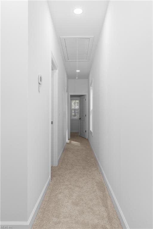 corridor with light colored carpet, attic access, and baseboards