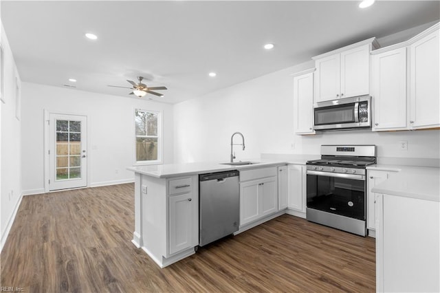 kitchen featuring dark wood finished floors, light countertops, appliances with stainless steel finishes, a peninsula, and a sink