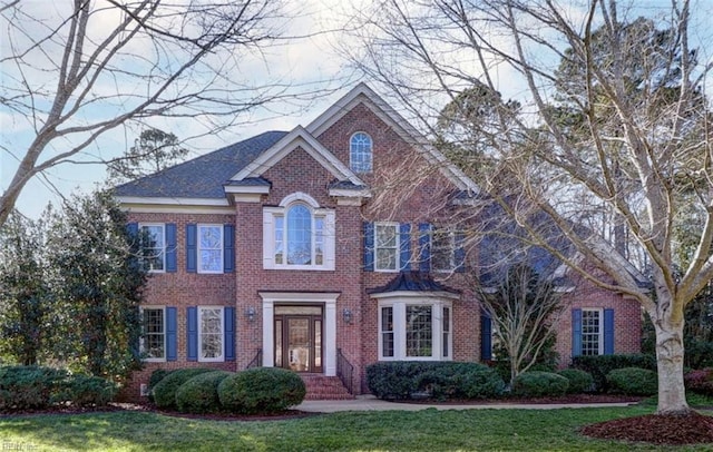 view of front of property featuring brick siding, roof with shingles, and a front yard