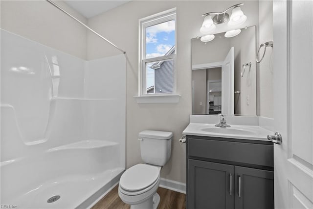 bathroom with a shower, toilet, vanity, wood finished floors, and baseboards