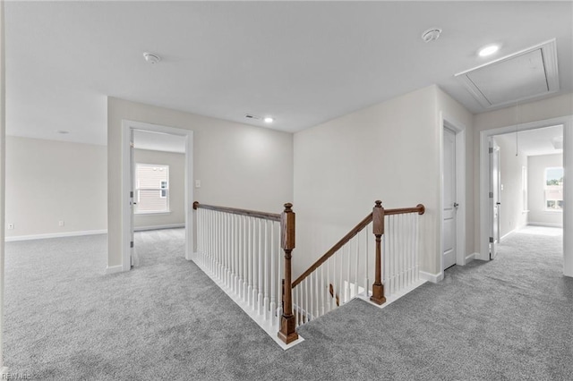 hall featuring attic access, carpet, baseboards, and an upstairs landing