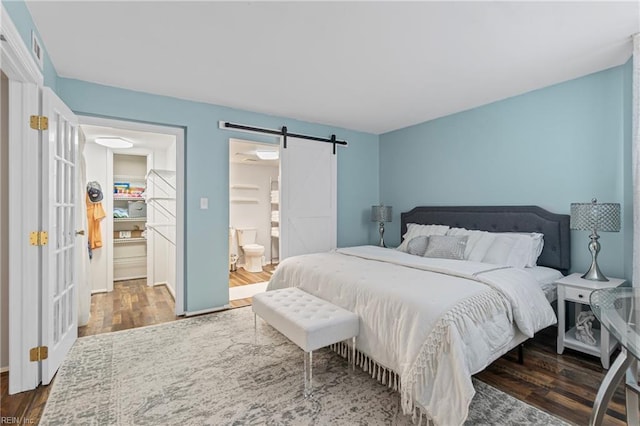 bedroom featuring ensuite bath, a walk in closet, a barn door, and wood finished floors