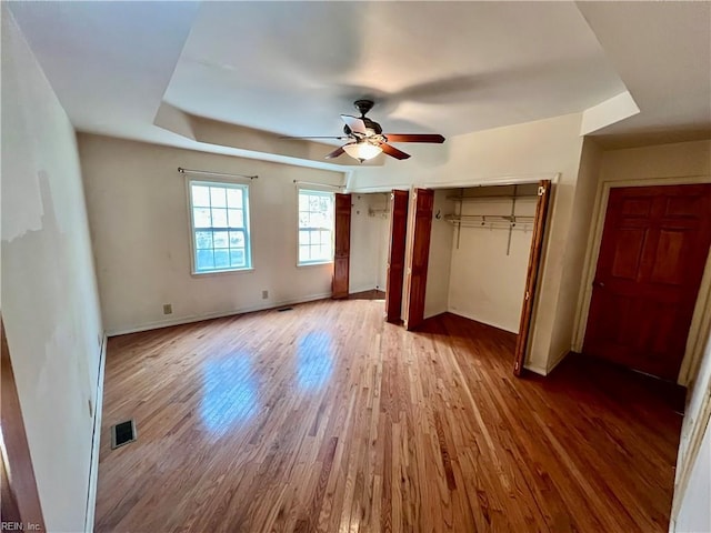 unfurnished bedroom featuring ceiling fan, wood finished floors, visible vents, baseboards, and two closets