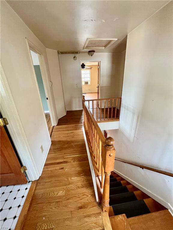 corridor with light wood-style flooring, baseboards, attic access, and an upstairs landing