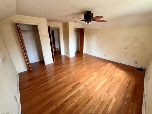 unfurnished bedroom featuring multiple closets, a ceiling fan, vaulted ceiling, and wood finished floors