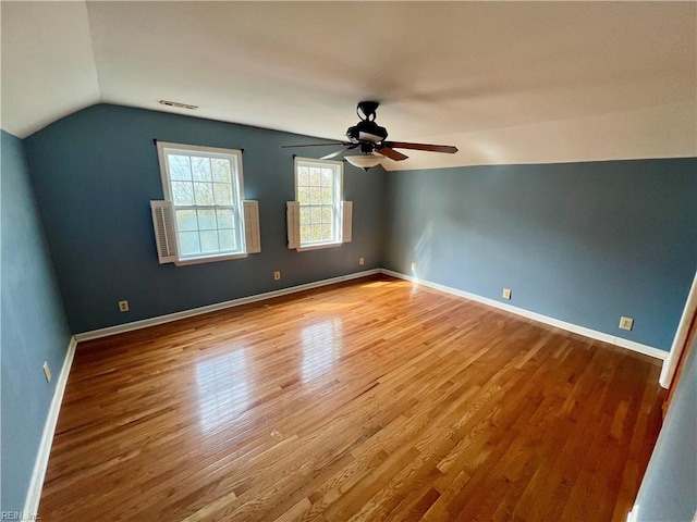 spare room featuring lofted ceiling, visible vents, baseboards, and wood finished floors