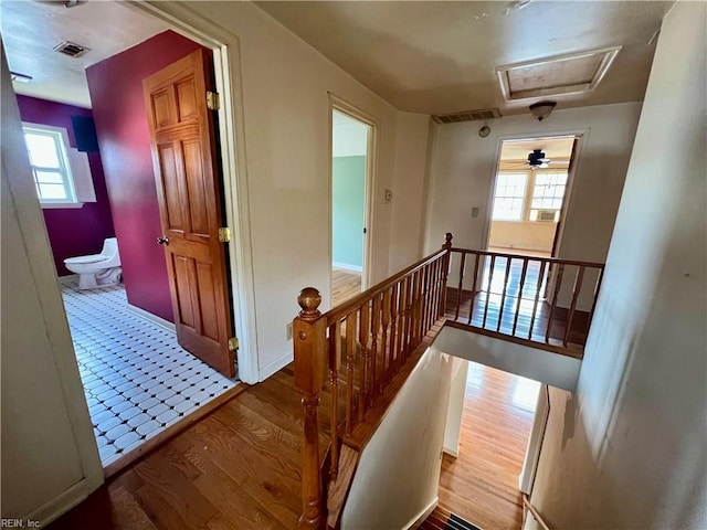 hall with visible vents, wood finished floors, and an upstairs landing