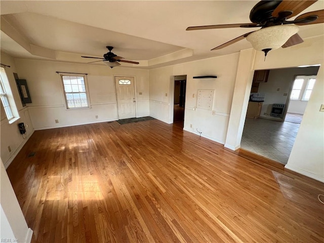 unfurnished living room with ceiling fan, wood finished floors, a raised ceiling, and a wealth of natural light