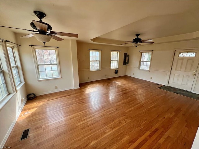 interior space featuring baseboards, visible vents, a ceiling fan, a raised ceiling, and wood finished floors