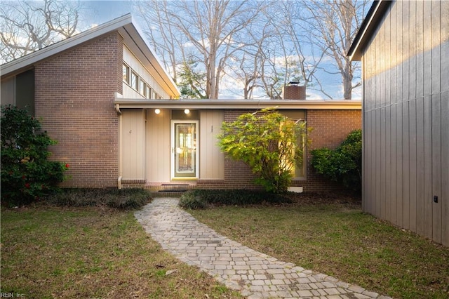 exterior space featuring a yard, brick siding, and a chimney