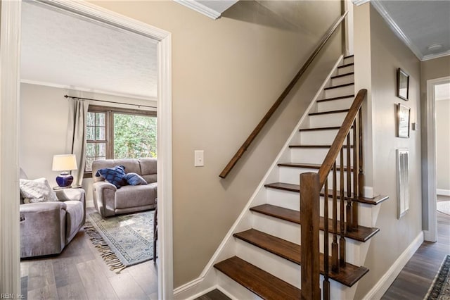 stairs with wood finished floors, baseboards, and ornamental molding