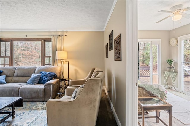 living room with baseboards, a textured ceiling, a ceiling fan, and crown molding