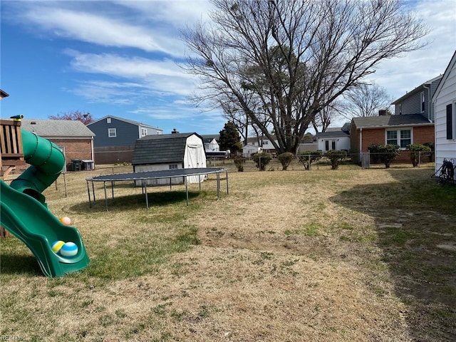 view of yard featuring a playground, a trampoline, fence, an outbuilding, and a storage unit