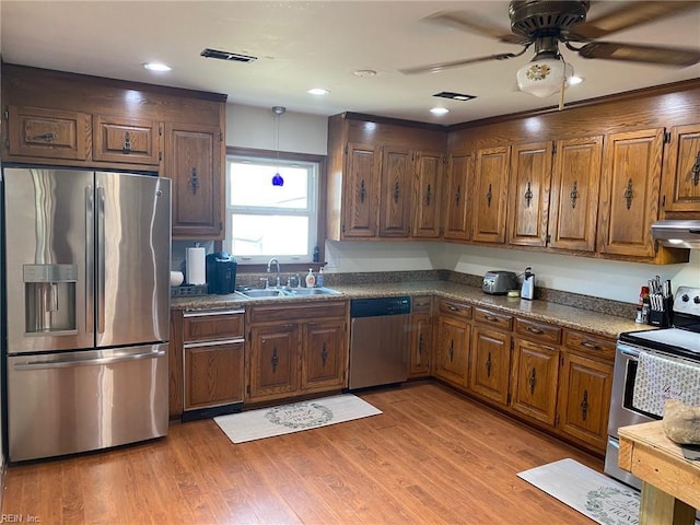 kitchen with a sink, stainless steel appliances, light wood-style floors, under cabinet range hood, and dark countertops