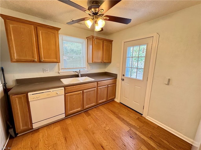 kitchen with white dishwasher, a sink, light wood-style floors, plenty of natural light, and dark countertops