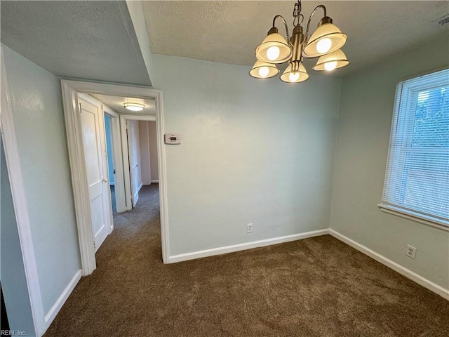 spare room with a textured ceiling, dark carpet, an inviting chandelier, and baseboards