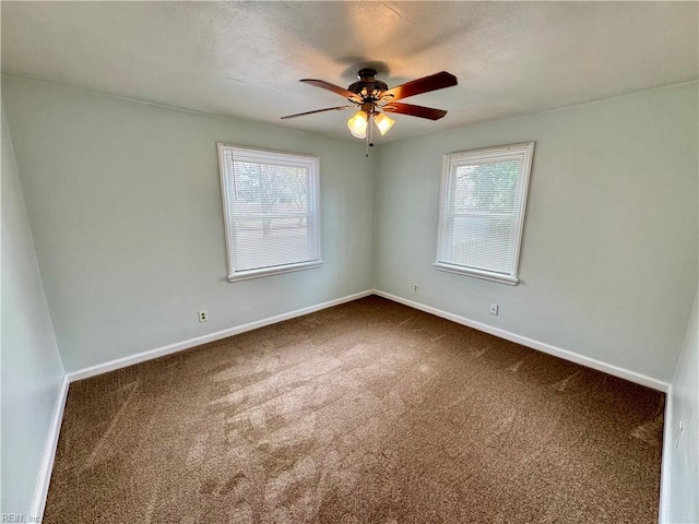 empty room with a textured ceiling, dark carpet, a ceiling fan, and baseboards