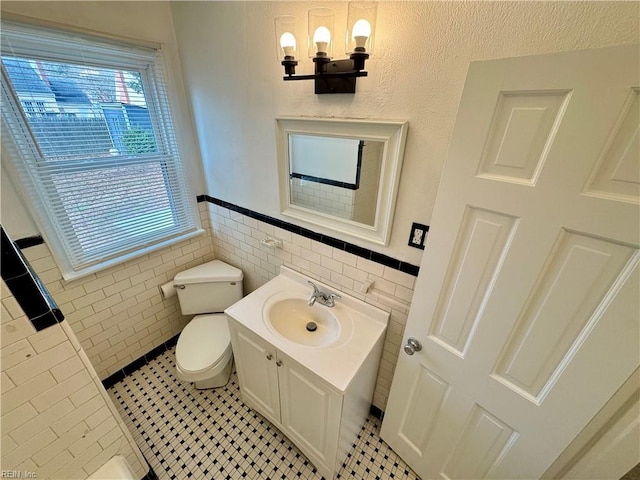 bathroom featuring toilet, tile patterned floors, an inviting chandelier, vanity, and tile walls