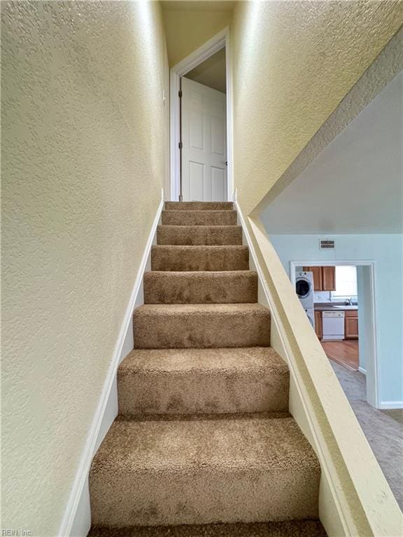 stairway featuring a textured wall, carpet floors, visible vents, baseboards, and washer / clothes dryer