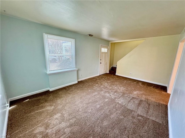 carpeted empty room featuring stairway and baseboards