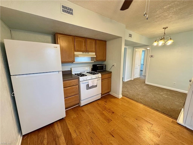 kitchen with brown cabinets, visible vents, light wood-style flooring, white appliances, and under cabinet range hood