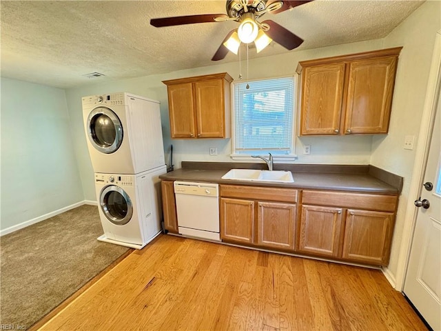 clothes washing area featuring stacked washer / drying machine, light wood-style flooring, a sink, a textured ceiling, and laundry area