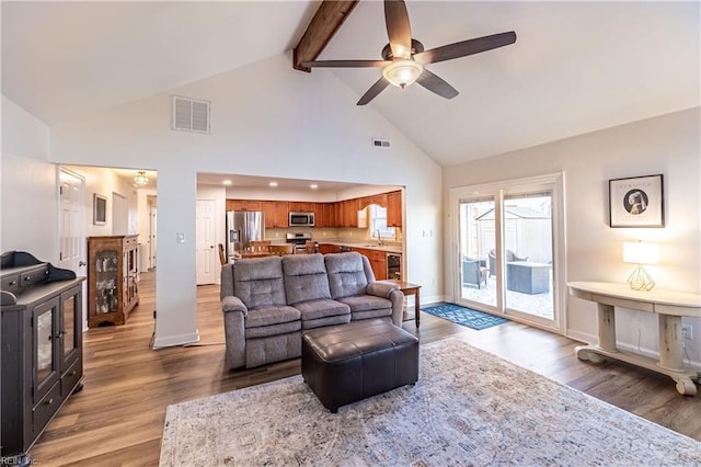 living room with ceiling fan, visible vents, wood finished floors, and beamed ceiling