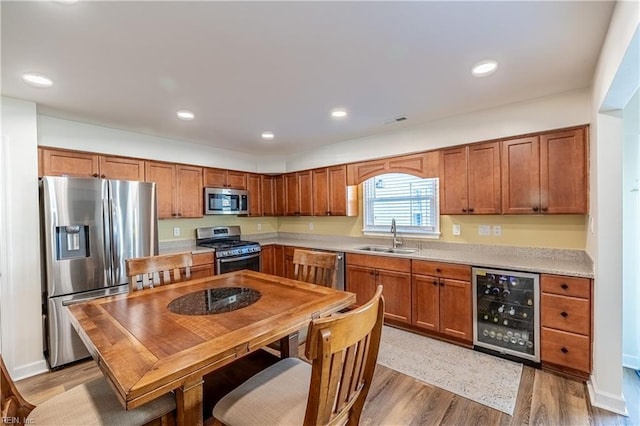 kitchen featuring light countertops, light wood-style flooring, appliances with stainless steel finishes, a sink, and beverage cooler