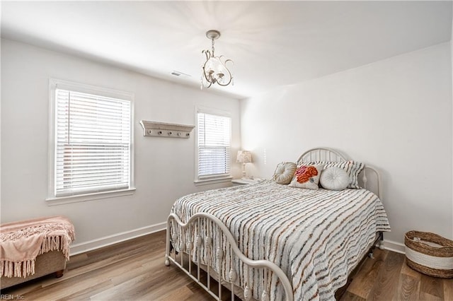 bedroom featuring visible vents, baseboards, a chandelier, and wood finished floors