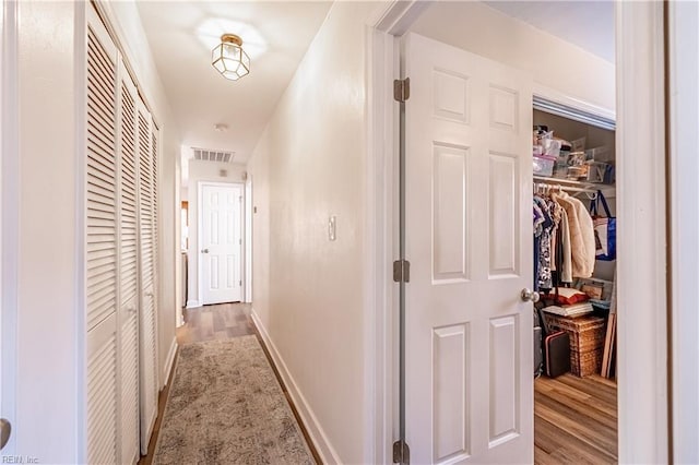 hall featuring baseboards, visible vents, and wood finished floors