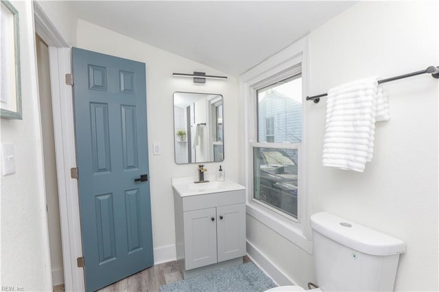 bathroom with lofted ceiling, toilet, vanity, wood finished floors, and baseboards