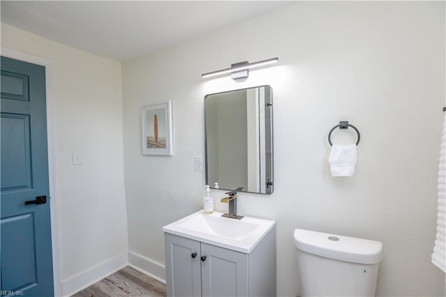 half bathroom with baseboards, vanity, toilet, and wood finished floors