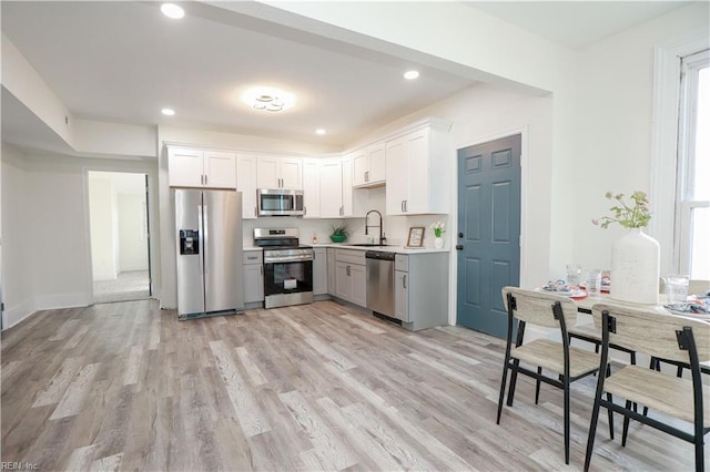 kitchen with light wood finished floors, recessed lighting, light countertops, appliances with stainless steel finishes, and a sink