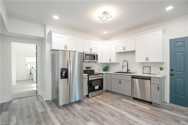 kitchen with light countertops, light wood-style flooring, appliances with stainless steel finishes, white cabinets, and a sink