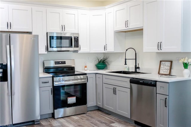 kitchen featuring gray cabinetry, stainless steel appliances, a sink, light wood-style floors, and light countertops