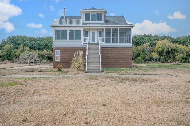 coastal home featuring stairway, a front lawn, and a sunroom